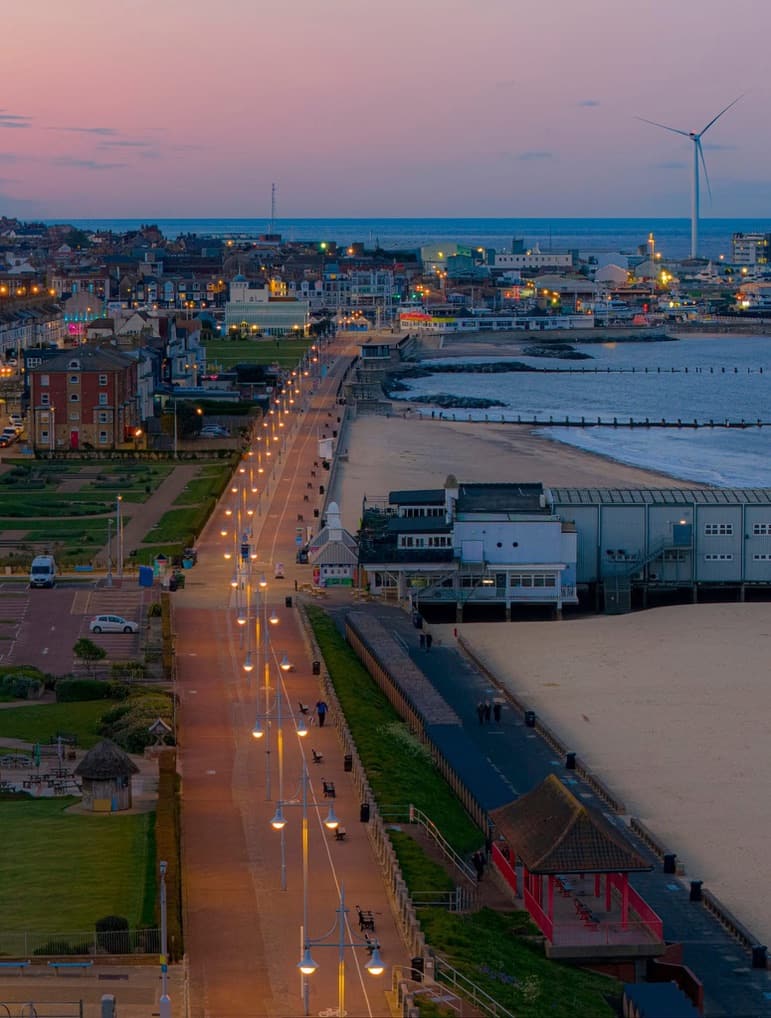 Lowestoft seafront at dusk, with the promenade lit up beside the beach and the wind turbine on the horizon