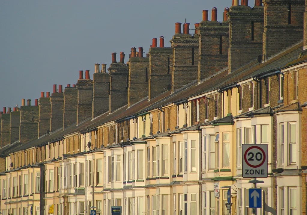 A long terrace of Victorian townhouses with rows of chimney pots, lit by golden evening sun